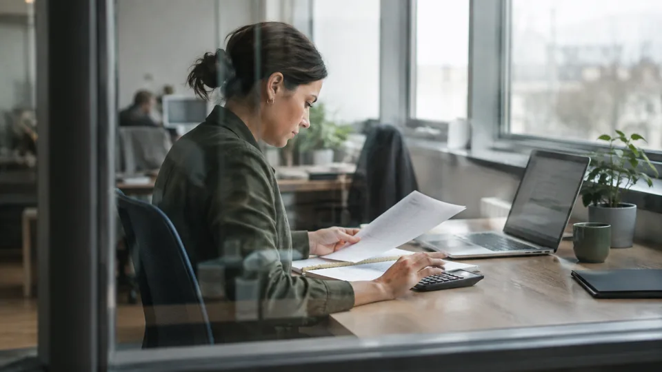 Operations manager comparing automation review notes with a time log and a simple calculator.